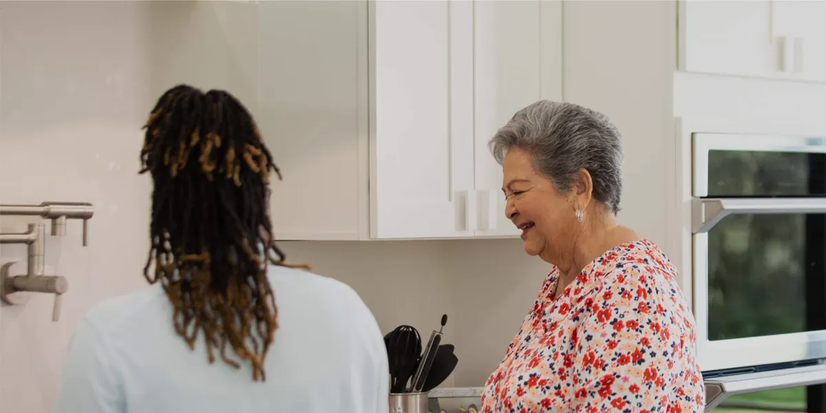 A caregiver and an older woman laughing in her kitchen
